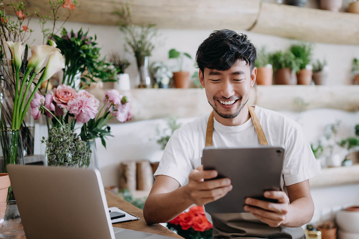 Smiling Asian male florist looks at tablet