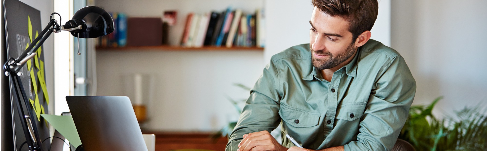 Young Man Using Laptop at Desk on Sunny Day