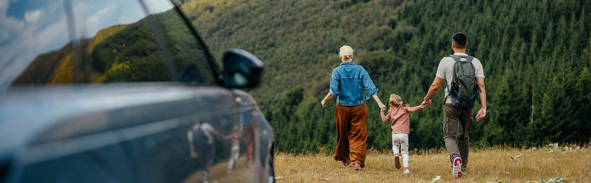 Family Walking on Hillside with Parked Car in the Foreground