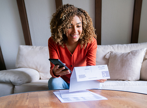 Person reviewing a bill and mobile phone while managing monthly bill payments.