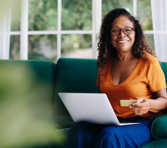 Woman Smiling and Using Credit Card and Laptop on Sofa