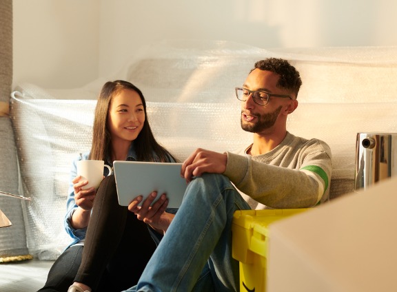 Couple Sitting on Floor Using Tablet and Drinking Coffee