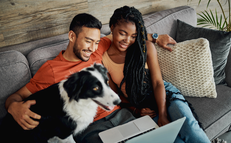 Man, Woman and Dog on Sofa Looking at Laptop