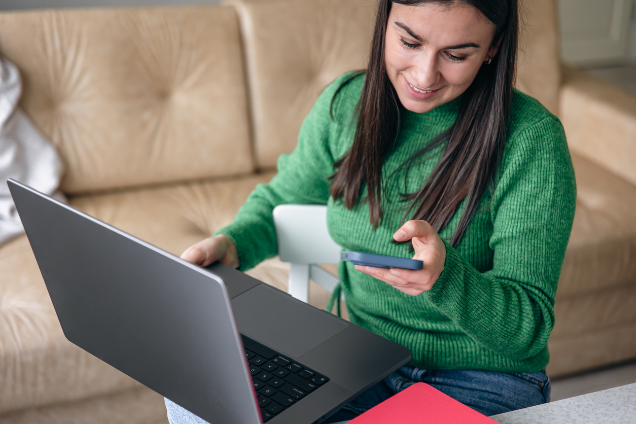 Woman Using Phone and Laptop on Sofa