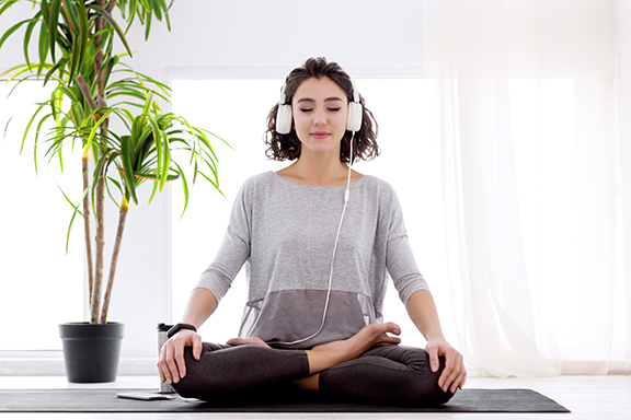 Woman Meditating while Wearing Headphones and Sitting in Front of Potted Plant